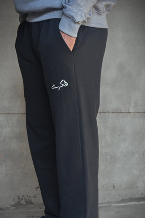 Person wearing black sweatpants with a logo against a concrete wall.