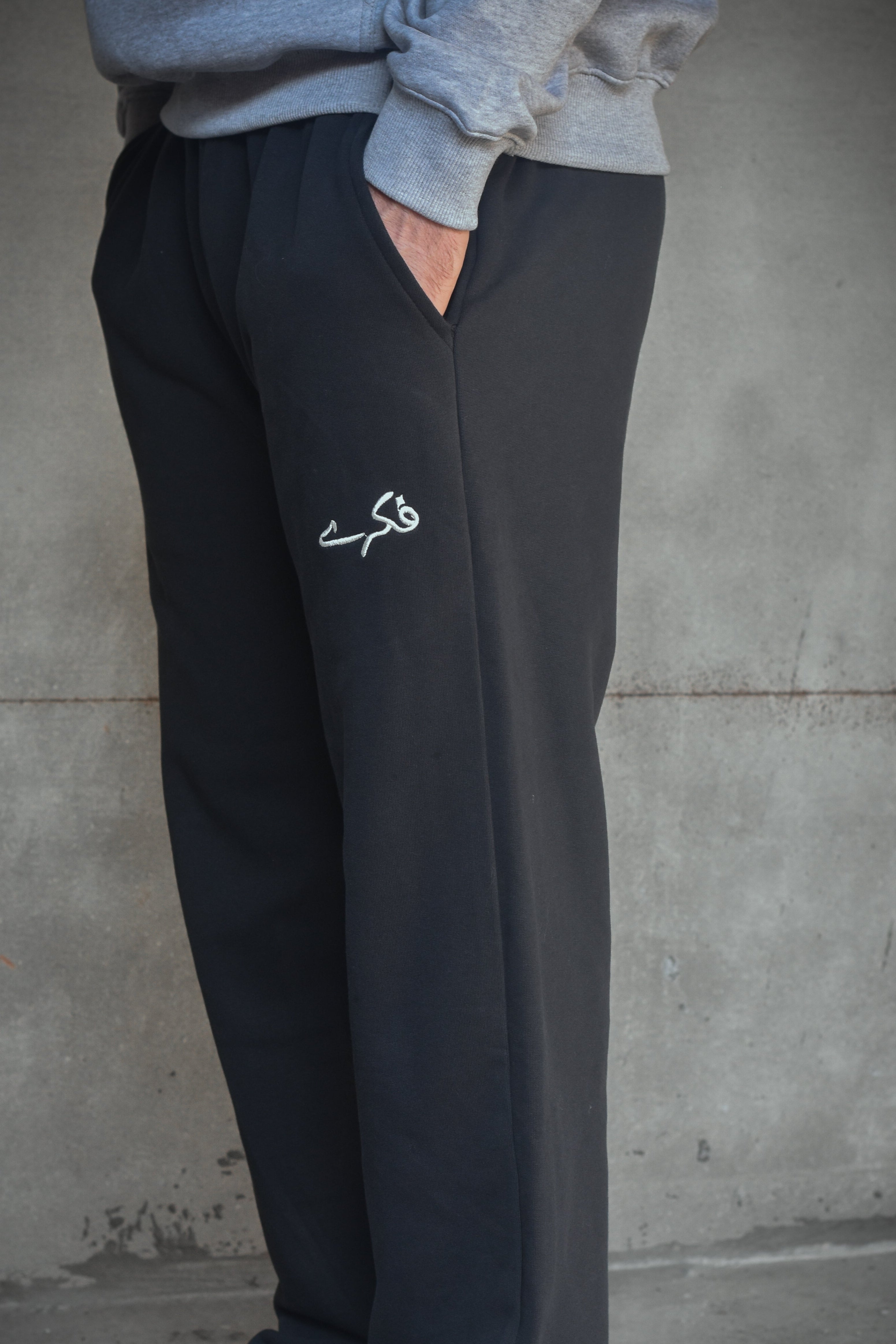 Person wearing black sweatpants with a logo against a concrete wall.